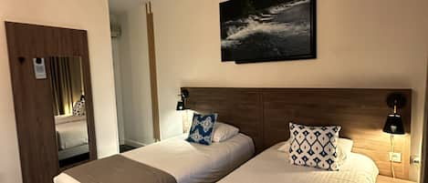 A hotel room with two beds, a mounted TV, a door, and a mirror.