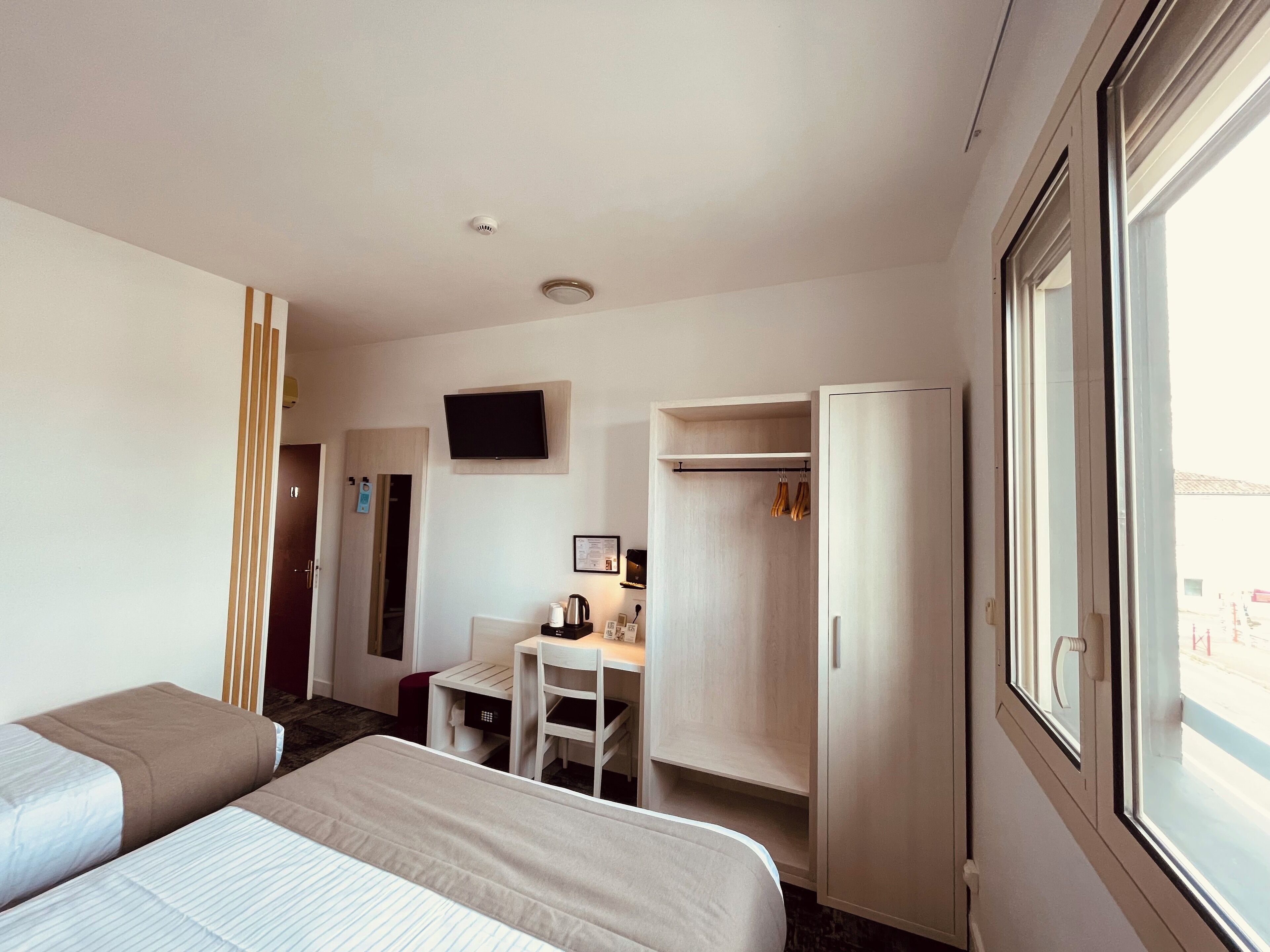A hotel room with two beds, a desk, a TV, and a wardrobe.