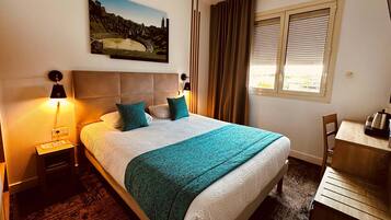Una habitación de hotel con cama, escritorio, ventana con persianas, un cuadro en la pared y mesita de noche con lámpara.