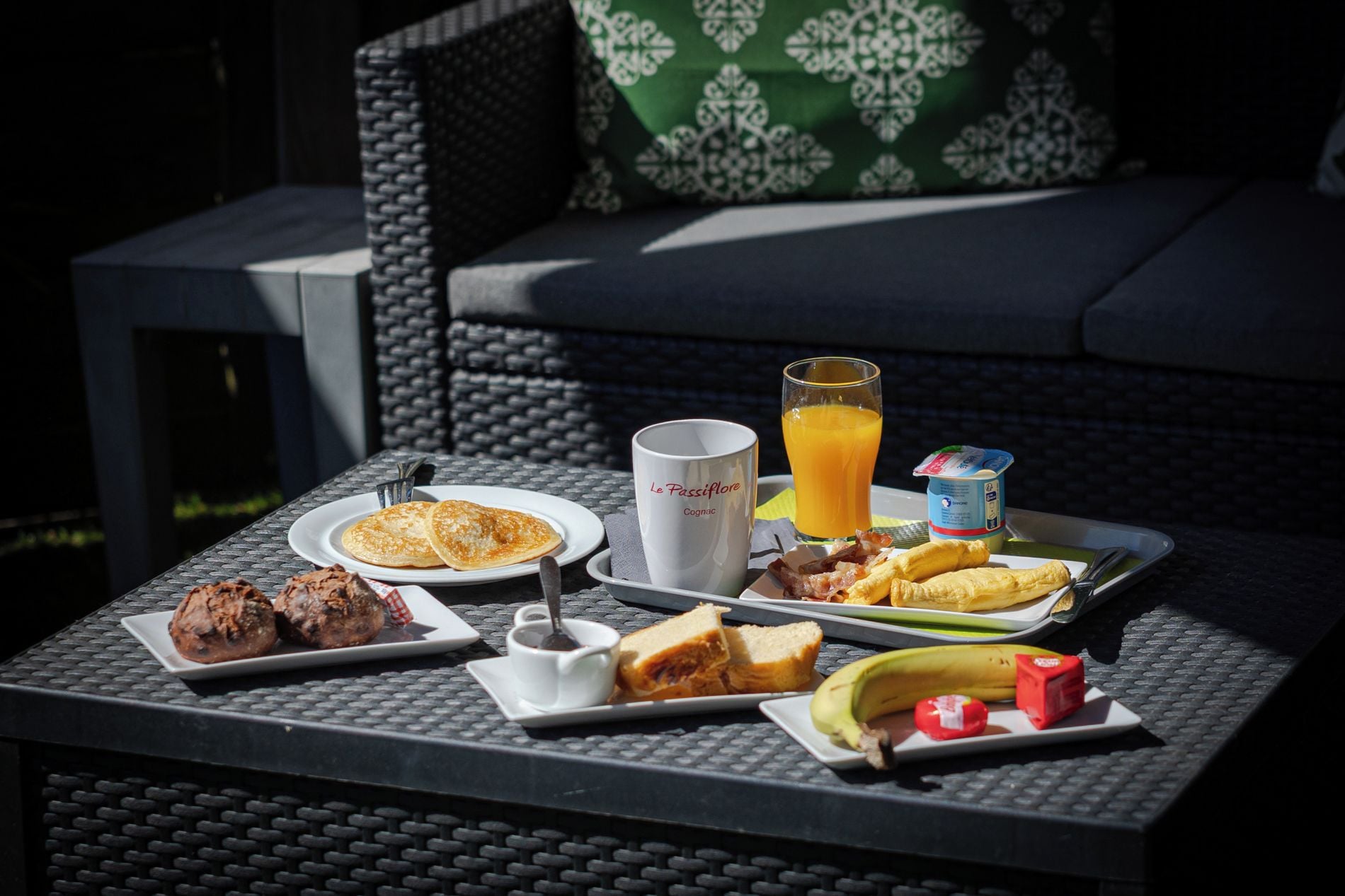 A breakfast tray with pancakes, bacon, eggs, toast, a glass of orange juice, and a coffee mug on a table.