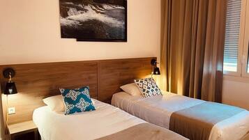 A hotel room with two beds, a wooden headboard, a nightstand, a lamp, and a painting on the wall.