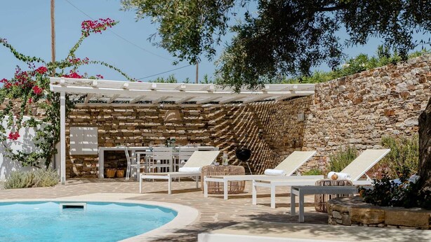 A poolside area with lounge chairs, a pergola, and a stone wall.