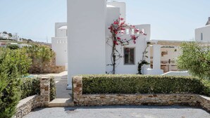 A white building with a stone wall and a hedge in front.