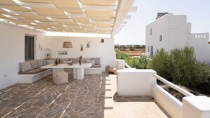 A sunlit patio with a stone floor, white furniture, and a view of the surrounding landscape.