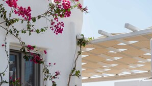 A white building with pink bougainvillea vines climbing up the wall and a white pergola structure.