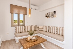 A modern living room with a sectional sofa, a wooden coffee table, and a window with a view. - Villa Rocabella – Just 100m from Glyfada Beach (Naxos)