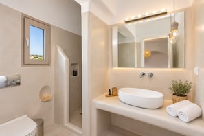 Un baño con un espejo grande, un lavamanos blanco, una ducha y un ventanal con vistas.