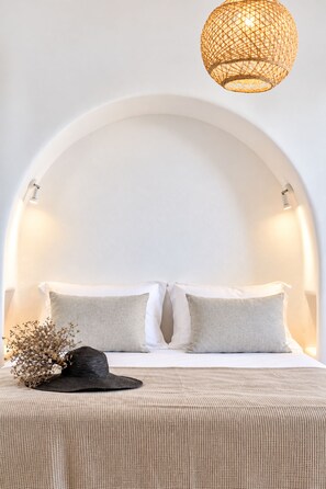 A bed with a white headboard, two pillows, a dark hat, and a woven light fixture above. - Villa Rocabella – Just 100m from Glyfada Beach (Naxos)