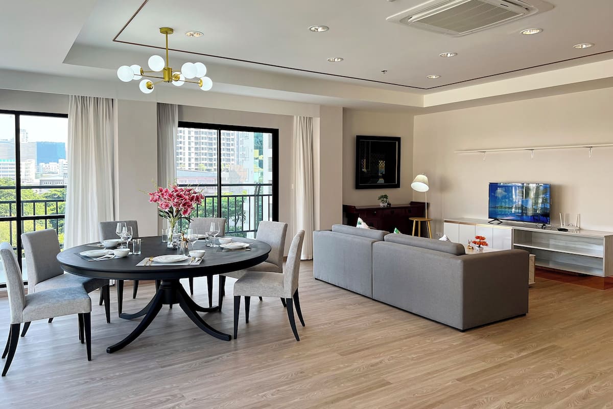 A modern living room with a round dining table, grey sofa, and a large TV.