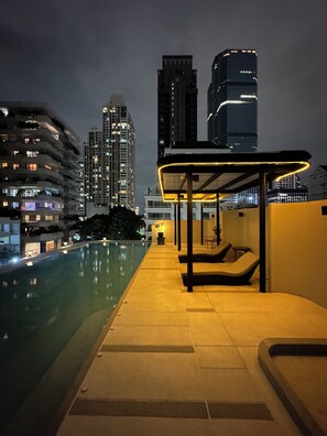 A nighttime view of a swimming pool area with a covered seating area and high-rise buildings in the background. - Sathorn 111 (Bangkok)