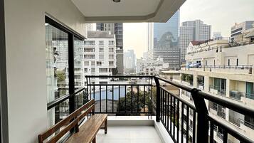 A balcony with a wooden bench, a view of the cityscape, and a tiled floor.