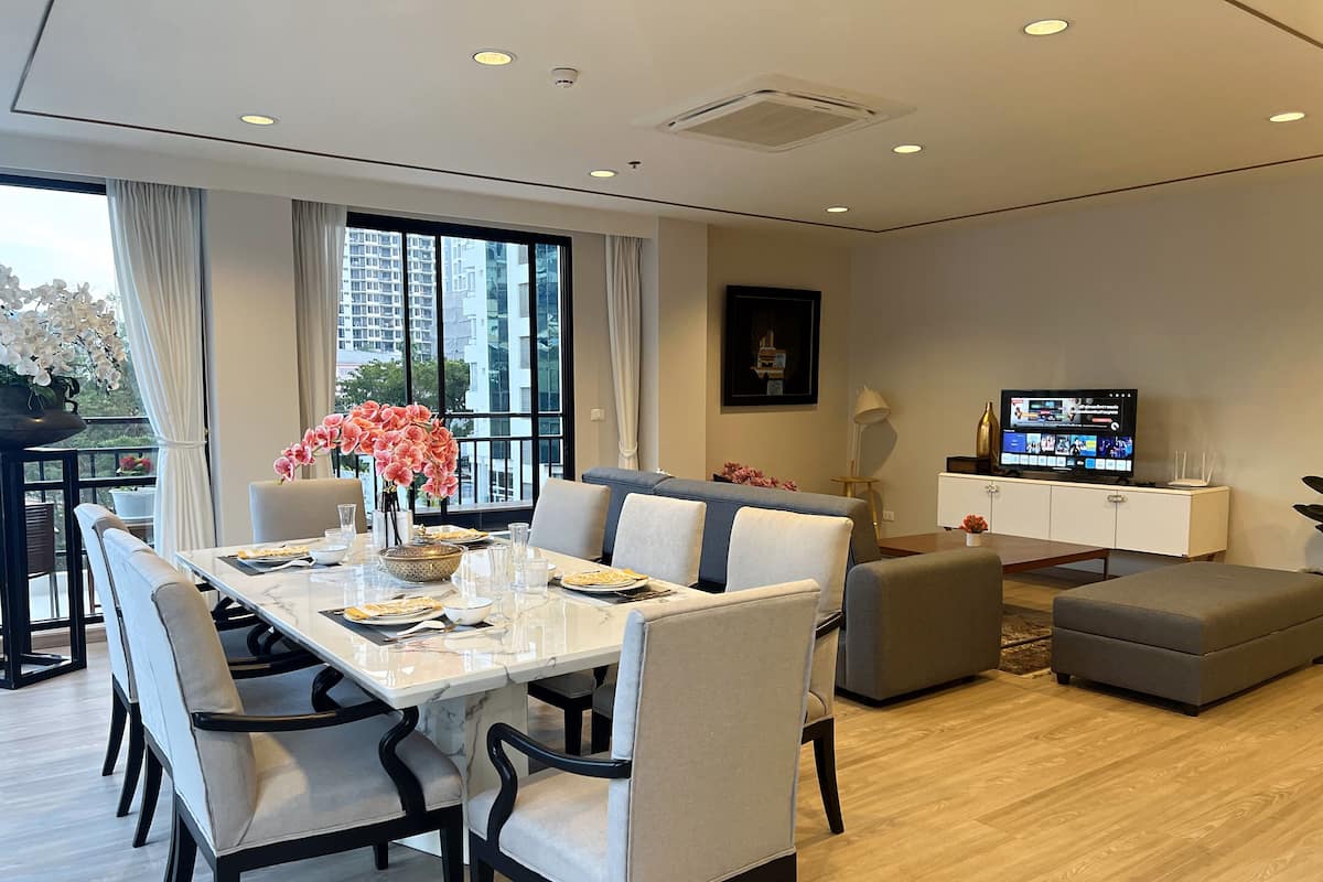 A modern living room with a dining area, a sofa, a TV, and a balcony with a view of buildings.