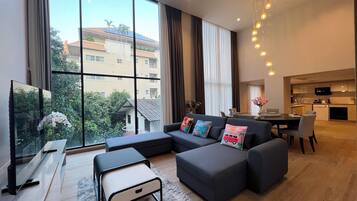 A modern living room with a sectional sofa, a flat-screen TV, and a dining area with a table and chairs.