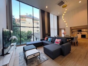 A modern living room with a sectional sofa, a flat-screen TV, and a dining area with a table and chairs. - Sathorn 111 (Bangkok)