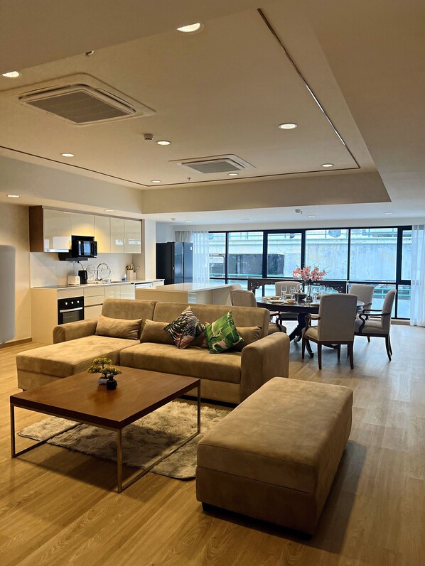 A modern living room with a sofa, ottoman, and coffee table, a dining area with chairs and a table, and a kitchen with appliances. - Sathorn 111 (Bangkok)