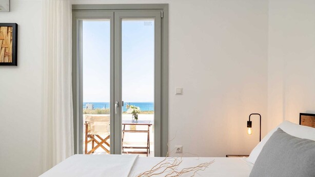 Une chambre d’hôtel avec un lit, une table de chevet, une lampe et une vue sur la mer, accessible par une porte coulissante.