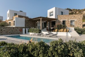 A modern villa with a pool, outdoor seating, and stone walls.