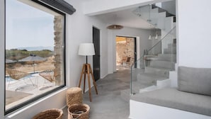 A modern interior with a staircase, a sofa, wicker baskets, and a view of an outdoor area with umbrellas. - Villa Andalusia, Orkos Naxos (Naxos)
