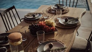 A dining table set with plates, glasses, and a centerpiece of grapes and nuts by a pool. - Villa Andalusia, Orkos Naxos (Naxos)