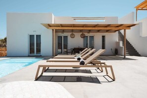 A modern outdoor pool area with sun loungers, a covered seating area, and a staircase leading to an upper level. - Villa Solena, Agia Anna (Naxos)