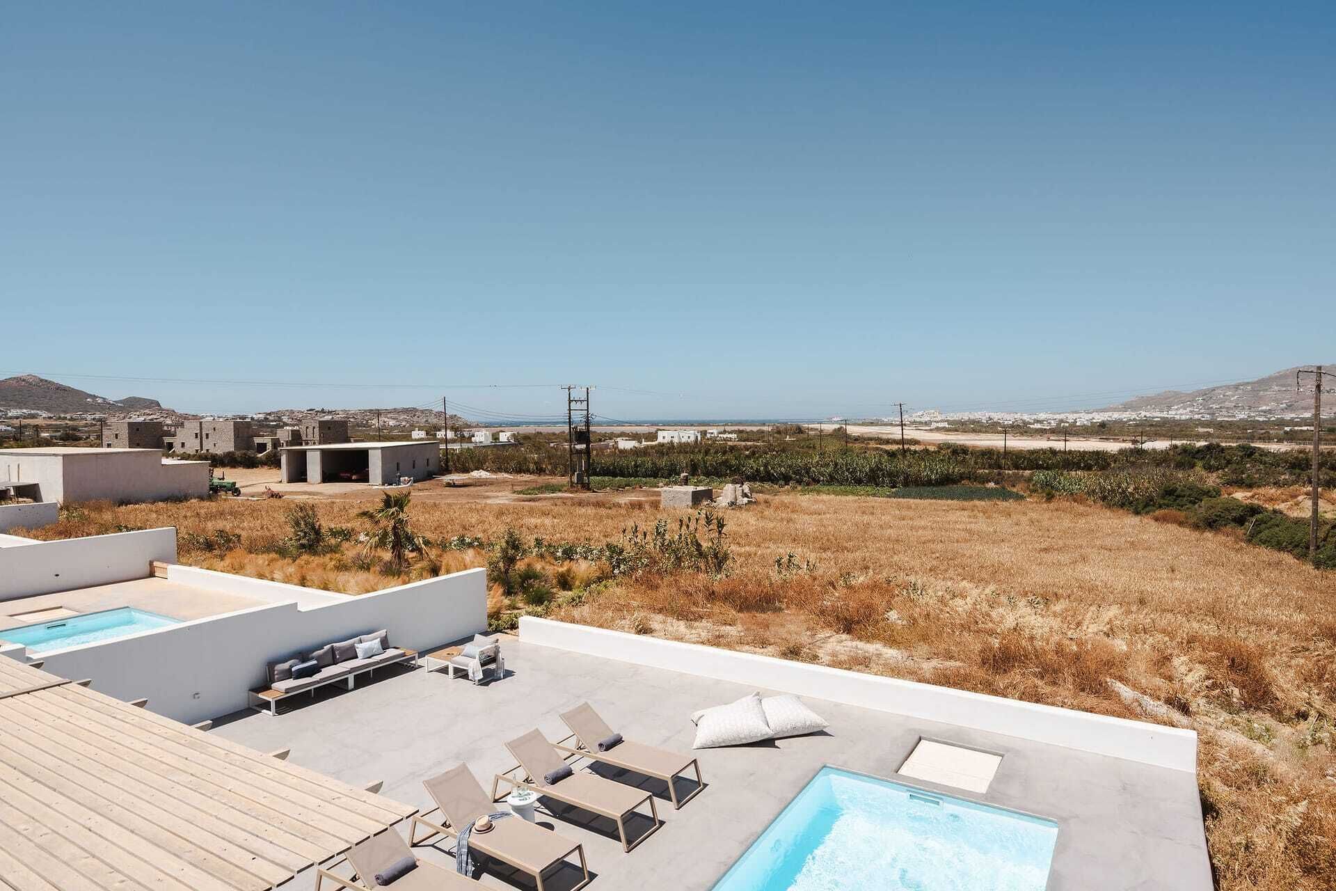 A rooftop pool area with lounge chairs and a swimming pool, surrounded by dry grass and a clear view of distant buildings and hills.