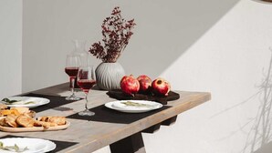 Une table à manger avec des assiettes remplies de nourriture, des verres de vin rouge et un vase contenant des fleurs séchées.