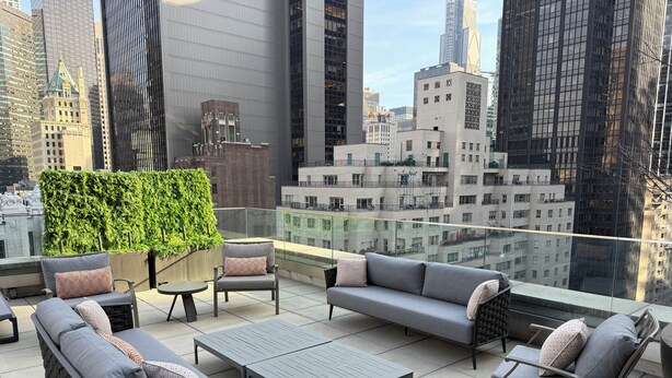 A rooftop terrace with a sofa, chairs, and a table, surrounded by a cityscape view.