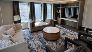 A modern hotel room with a sofa, a round coffee table, a TV, and a bookshelf.