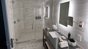 A modern bathroom with a large mirror, two sinks, a shower, and a bench.