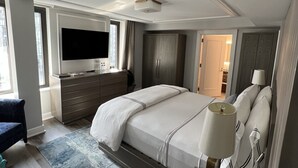 A modern hotel room with a large bed, a flat-screen TV, a desk with a lamp, and a view of the city through the window.