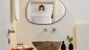 A modern bathroom with a large, rustic vessel sink, a round mirror, and a wall-mounted light fixture. - Villa Ama , Plaka Area , Naxos (Naxos)
