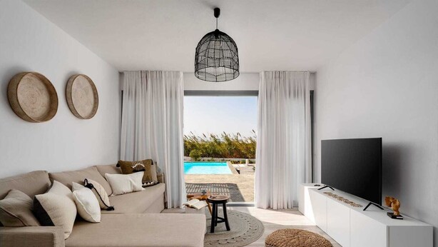 Un soggiorno moderno con un divano color beige, una televisione a schermo piatto e vista su una piscina.