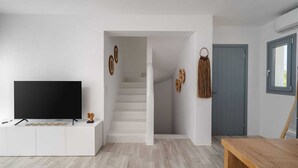 Un soggiorno moderno con una televisione a schermo piatto su una console bianca, una scala che conduce a un'altra stanza e un tavolo da pranzo in legno.