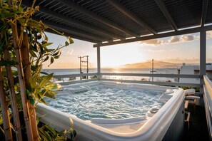 Een hottub met uitzicht op de ondergaande zon boven de oceaan, omringd door bamboeplanten.