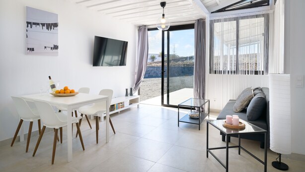 Ein modernes Wohnzimmer mit Essbereich, einer Couch, einem Fernseher und Blick ins Freie.