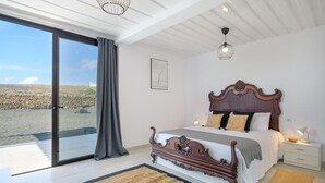 Ein Schlafzimmer mit einem großen Bett, einem Nachttisch, einer Lampe und Blick ins Freie.
