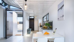 Eine moderne Küche mit weißen Schränken, ein Essbereich mit weißem Tisch und Stühlen sowie ein großes Fenster, das für natürliches Licht sorgt.