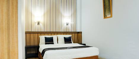 A neatly arranged hotel room with a large bed, a wooden headboard, and two wall-mounted lights.