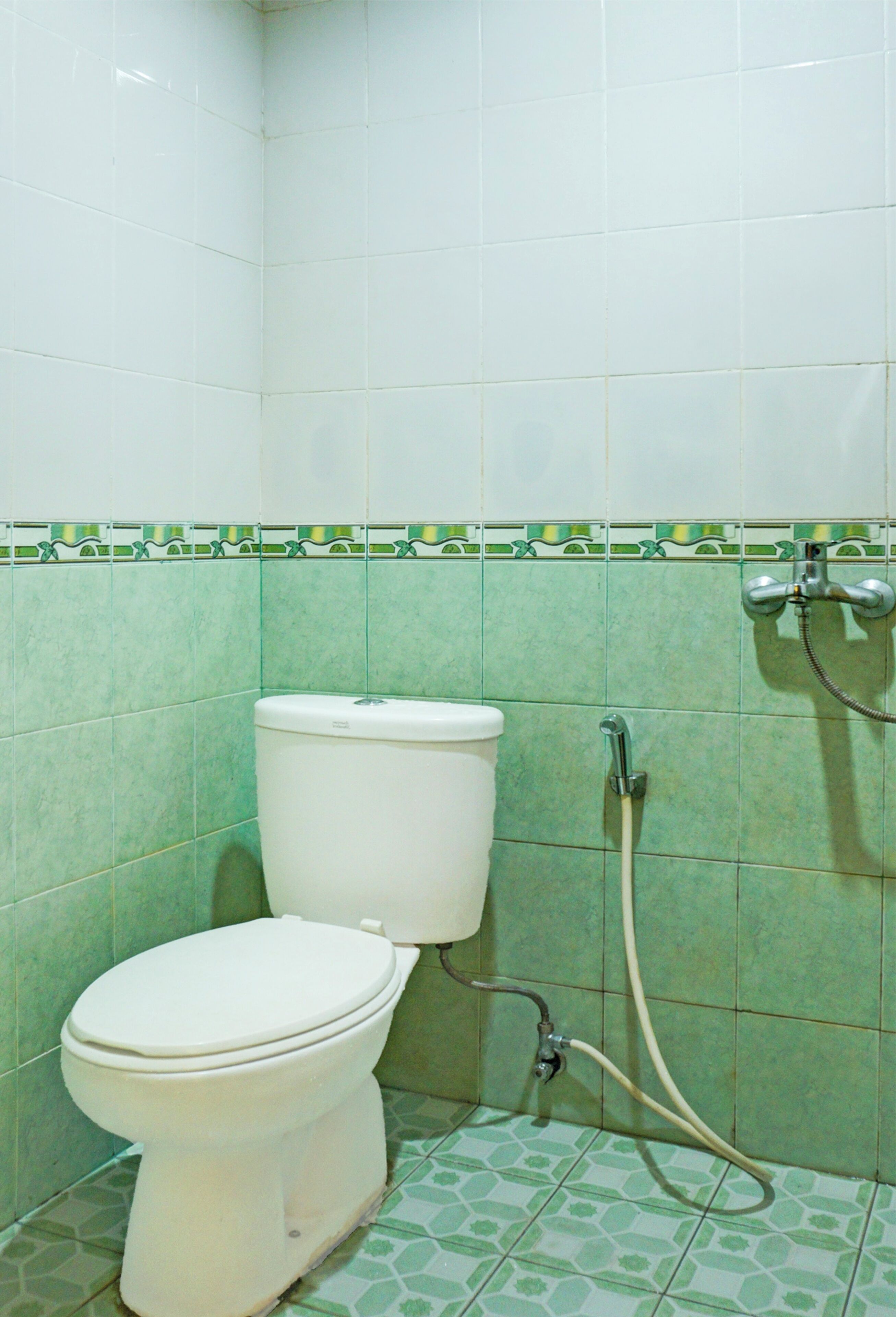 Une salle de bain avec des toilettes, une douche et des carreaux verts à motifs.