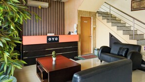 A reception desk with a sign, a staircase, a sofa, and a small table with a plant. - Collection O R.Sukamto Near Palembang Trade Center Mall (Palembang)
