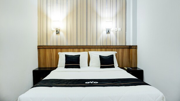 A hotel room with a bed, two bedside tables, a headboard with vertical stripes, and two wall-mounted lights. - Collection O R.Sukamto Near Palembang Trade Center Mall (Palembang)