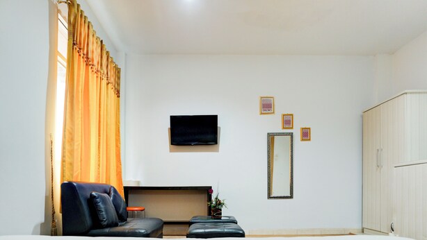 A hotel room with a bed, a sofa, a TV, a mirror, and a wardrobe.