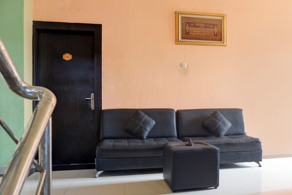 A black sofa with two cushions, a small ottoman, and a framed certificate on the wall. - Collection O R.Sukamto Near Palembang Trade Center Mall (Palembang)