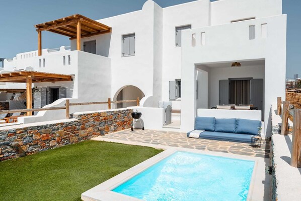 Un edificio moderno con pareti bianche e in pietra, una piscina e un'area relax esterna con mobili blu.