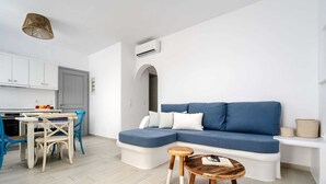 A modern living room with a blue sofa, a wooden coffee table, and a dining area with a blue chair and a white table.