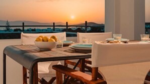 A dining table set with plates, glasses, and a bowl of lemons, overlooking a sunset view.