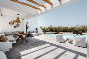 Un espacio exterior moderno con piscina, mobiliario blanco y una planta de cactus.