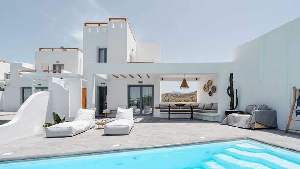 A modern poolside area with a pool, white walls, and a seating area with a view of the landscape.