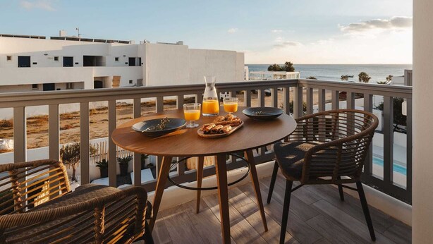 Un balcón con una mesa dispuesta para el desayuno, con vista a una playa y al océano.