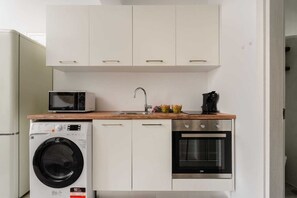 A compact kitchen with a washing machine, microwave, sink, and oven.